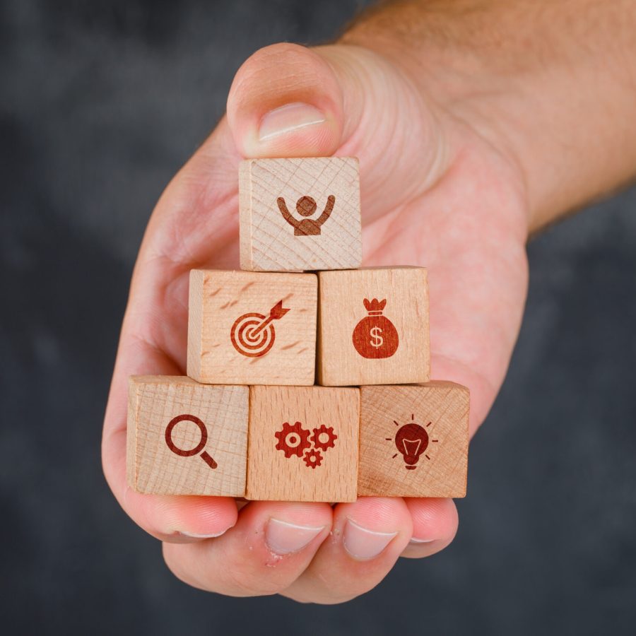 Business concept on grungy grey background side view. hand holding wooden blocks with icons.